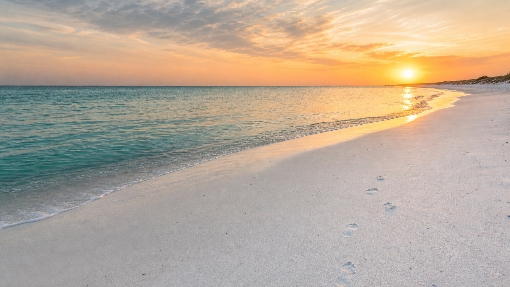 Empty pristine white sand beach in Destin Florida at early morning sunrise with no people, glassy calm emerald water, golden pink sky, footprints in the sand